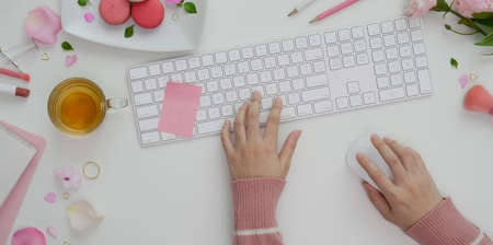 Overhead shot of young girl typing on keyboard in sweet pink feminine workspace with make up and office suppliesの写真素材