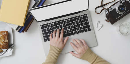 Top view of young female typing on laptop computer in cozy workspace with office supplies and bread の写真素材