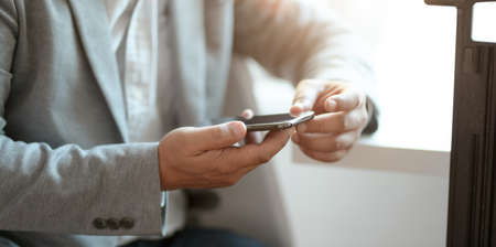 Close-up view of professional businessman looking at his smartphone while working at his workplaceの写真素材