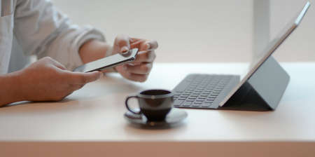 Close-up view of professional businessman looking at his smartphone while working at his workplaceの写真素材