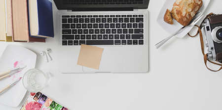 Overhead shot of cozy workspace with laptop computer, office supplies and painting tools on white...