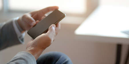 Close-up view of professional businessman looking at his smartphone while working at his workplaceの写真素材
