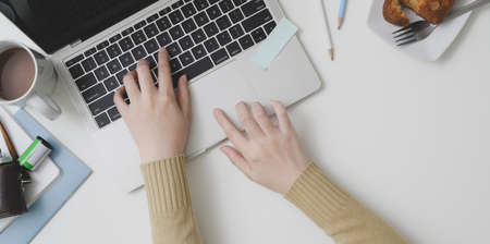 Overhead shot of young female typing on laptop computer in comfortable workspace with office suppliesの写真素材