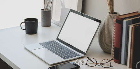 Minimal workspace with blank screen laptop computer, books, ceramic vase and office supplies の写真素材