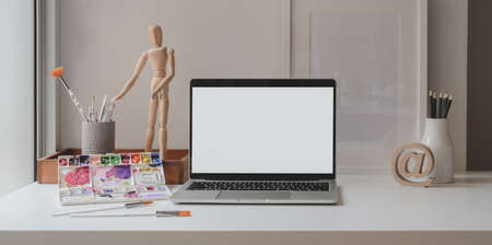 Comfortable artist workspace with blank screen laptop computer, painting tools and office supplies の写真素材