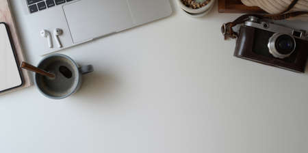 Overhead shot of comfortable workspace with laptop computer, camera, coffee cup and office supplies on white desk with copy spaceの写真素材