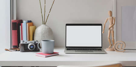 Open blank screen laptop computer with camera, books and coffee cup on white wooden table の写真素材