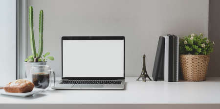 Comfortable workplace near the windows with open blank screen laptop computer with coffee cup and office supplies の写真素材