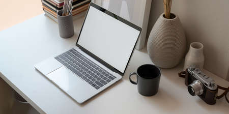 Minimal office room next to the windows with open blank screen laptop and office supplies の写真素材