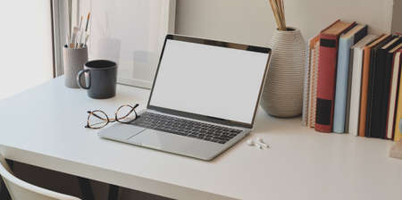 Minimal office room next to the windows with open blank screen laptop and office supplies の写真素材