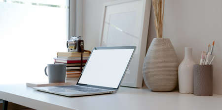 Minimal workspace with blank screen laptop computer, books, ceramic vase and office supplies の写真素材