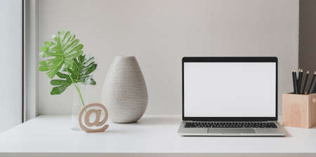 Open blank screen laptop computer in minimal workspace with tree pot, ceramic vase and copy space 
