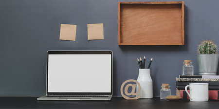 Open blank screen laptop computer in modern workspace with decorations and office supplies on black desk and grey wall background の写真素材