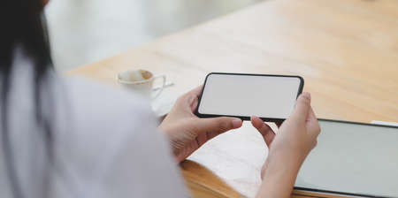 Close-up view of young female doctor looking at blank screen smartphone in her workspaceの写真素材