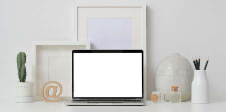 Minimal workspace with open blank screen laptop computer with mock up frames and ceramic vase decoration on white wall background の写真素材