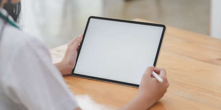 Cropped shot of young female doctor examining the patient chart while using tablet in her office roomの写真素材