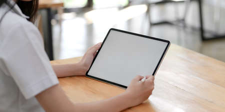Cropped shot of young female doctor examining the patient chart while using tablet in her office roomの写真素材