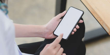 Close-up view of young female doctor touching blank screen smartphone in her office roomの写真素材