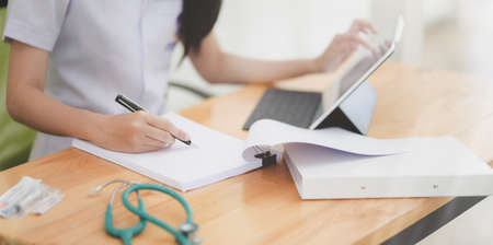 Cropped shot of young female doctor examining the patient chart while using tablet in her office roomの写真素材