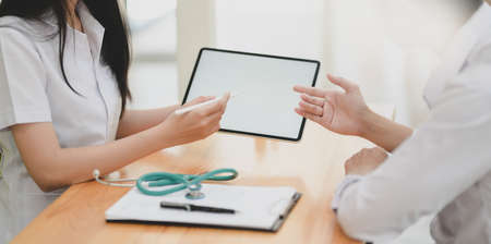 Cropped shot of young female doctor explain symptoms to her patient with digital tabletの写真素材