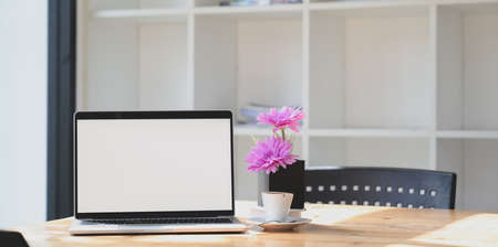 Open blank screen laptop computer in comfortable workspace with pink flower in tree pot の写真素材