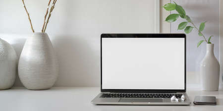 Open blank screen laptop computer in minimal workspace with copy space and ceramic vase decorations の写真素材