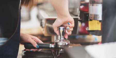 Cropped shot of professional female barista grinding fresh roasted coffee beans at coffee shop