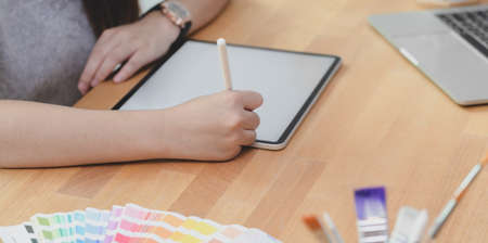 Close-up view of young female designer planing his project while tablet in her workplaceの写真素材