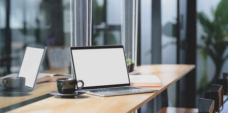 Comfortable workplace with open blank screen laptop computer on wooden table and black coffee cup の写真素材