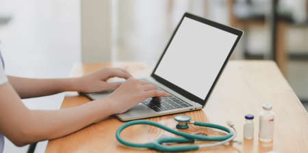 Close-up view of young female doctor examining the patient chart while using blank screen laptop computerの写真素材
