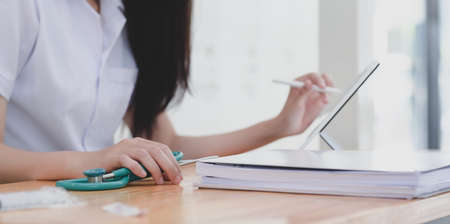 Close-up view of young female doctor examining the patient chart while using tablet in her workplaceの写真素材