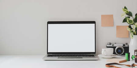 Mock up laptop computer in minimal workspace with copy space and office supplies on white table and white wall background の写真素材