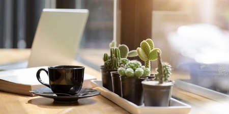 A cup of coffee with cactus in black pot in comfortable workplace with tablet in the background の写真素材