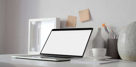 Minimal workspace with open blank screen laptop computer and mock up frame on white table and white wall の写真素材