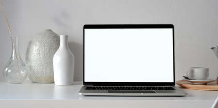 Open blank screen laptop computer in modern workspace with ceramic decorations and office supplies の写真素材