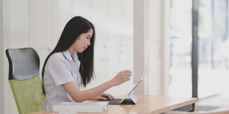 Young female doctor examining and analysing the patient chart with digital tablet in her office roomの写真素材