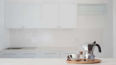 Coffee cup and Moka pot in wooden tray on white counter with blurred kitchen in the background の写真素材