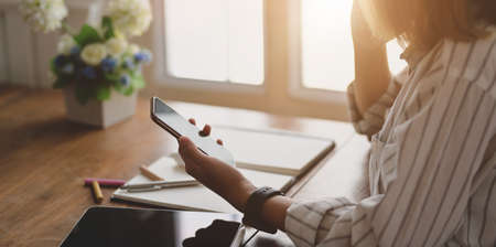 Close-up view of young female designer holding smartphone while working on her project in comfortable workspace の写真素材
