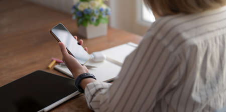 Close-up view of young female designer holding smartphone while working on her project in comfortable workspace の写真素材