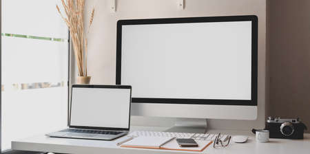 Blank screen desktop computer and laptop in modern workspace with office supplies の写真素材