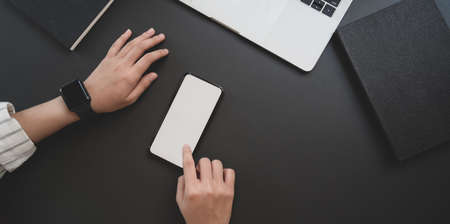 Top view of young businesswoman touching blank screen smartphone in dark luxury workspace with office supplies の写真素材
