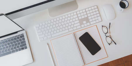 Cropped shot of modern workplace with open blank notebook, smartphone, keyboard computer and desktop computer with office supplies の写真素材