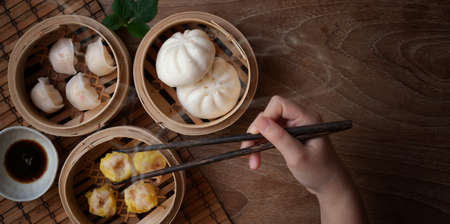 Overhead shot of woman eating Chinese steamed dumpling and steamed pork bun in a bamboo steamer with chopstickの写真素材