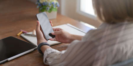 Close-up view of young female designer holding smartphone while working on her project in comfortable workspaceの写真素材
