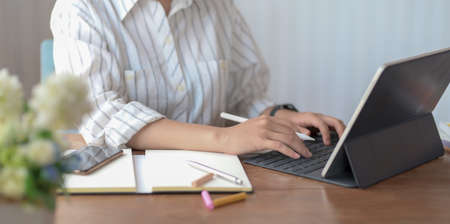 Cropped shot of young female designer typing on tablet while working on her projectの写真素材