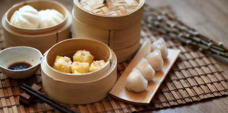 Cropped shot of Chinese steamed dumpling and steamed pork bun in a bamboo steamer on wooden tableの写真素材