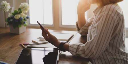 Close-up view of young female designer holding smartphone while working on her project in comfortable workspace の写真素材