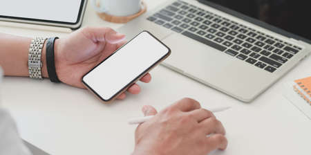 Close-up view of businessman surfing the internet on blank screen smartphone in his office roomの写真素材