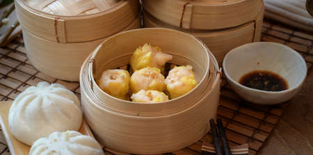 Chinese steamed dumpling and steamed pork bun in a bamboo steamer with chopstick on wooden tableの写真素材