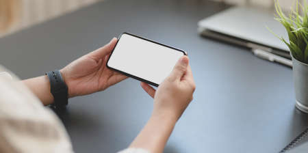 Cropped shot of professional businesswoman holding horizontal blank screen smartphone in his office roomの写真素材